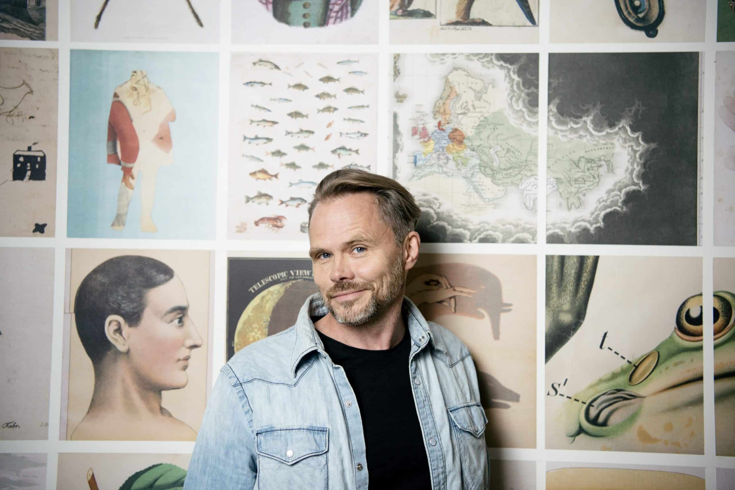 Mikael Genberg står foran en vegg med ulike kunstbilder.