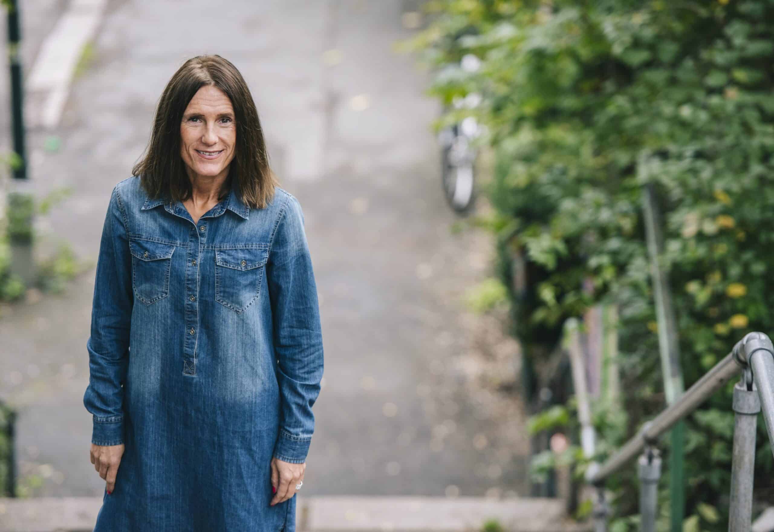 Kvinne i dongerikjole står og ser oppover, utendørs.