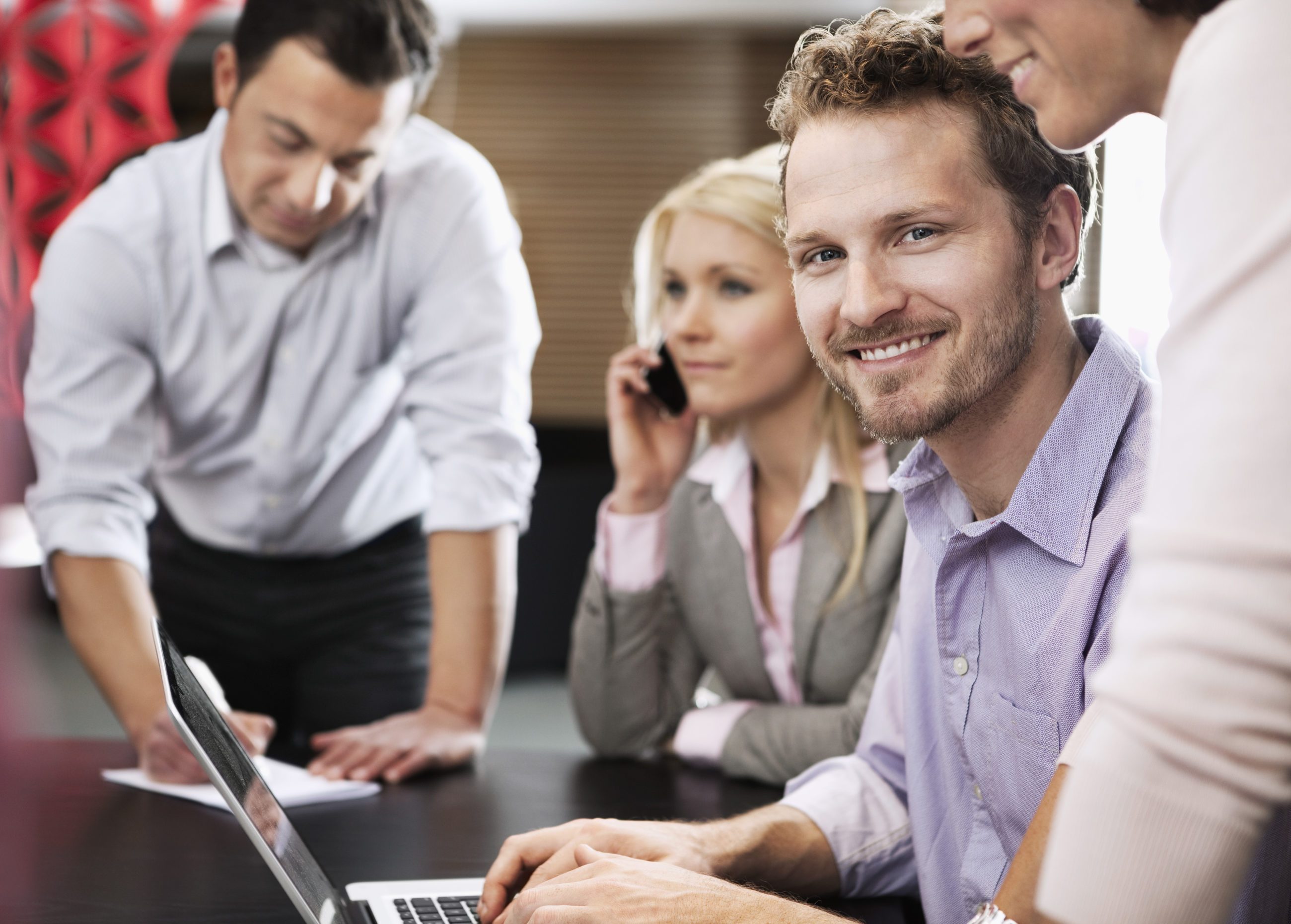Tre mennesker sitter sammen på jobb. Smilende mann i forgrunnen.