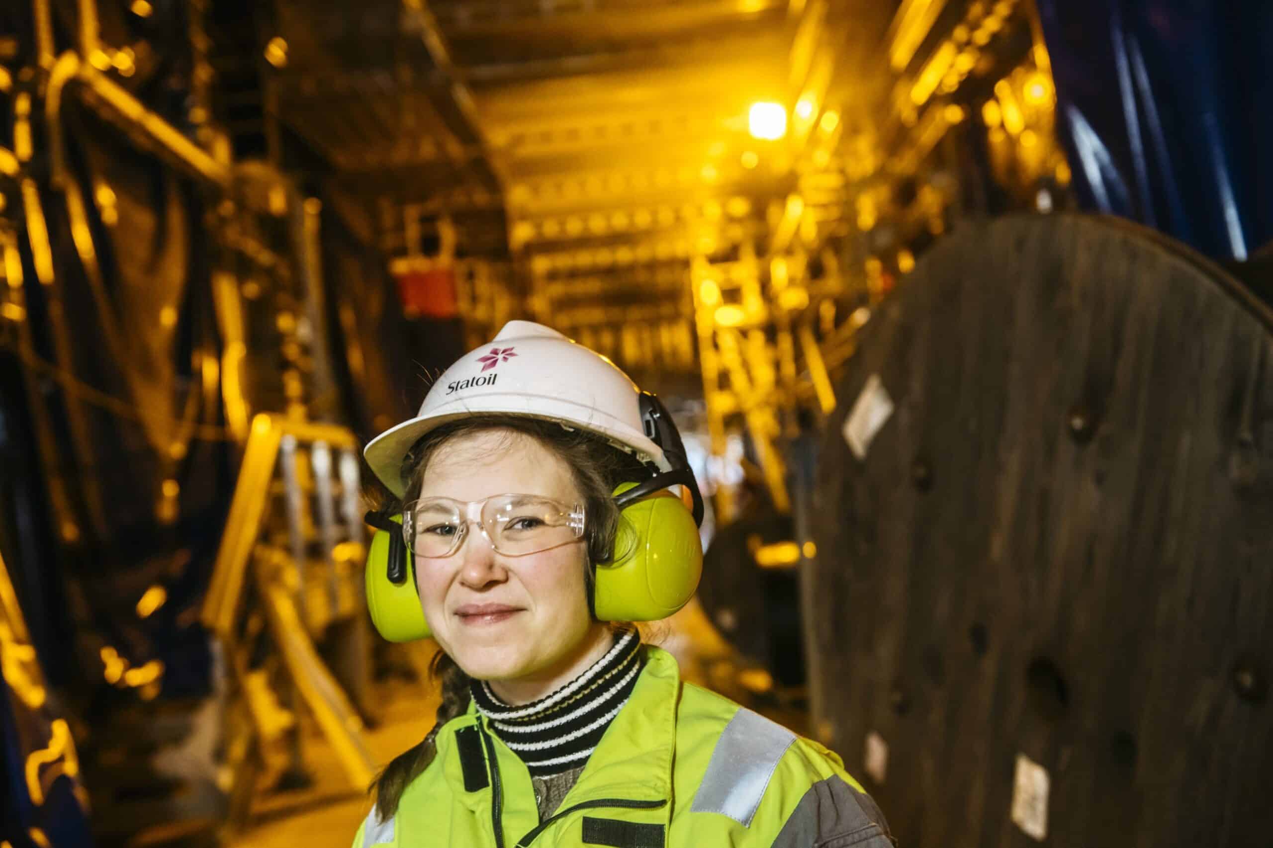 Ung kvinne med hørselvern, vernebriller og hjelm inne i en boligplattform.