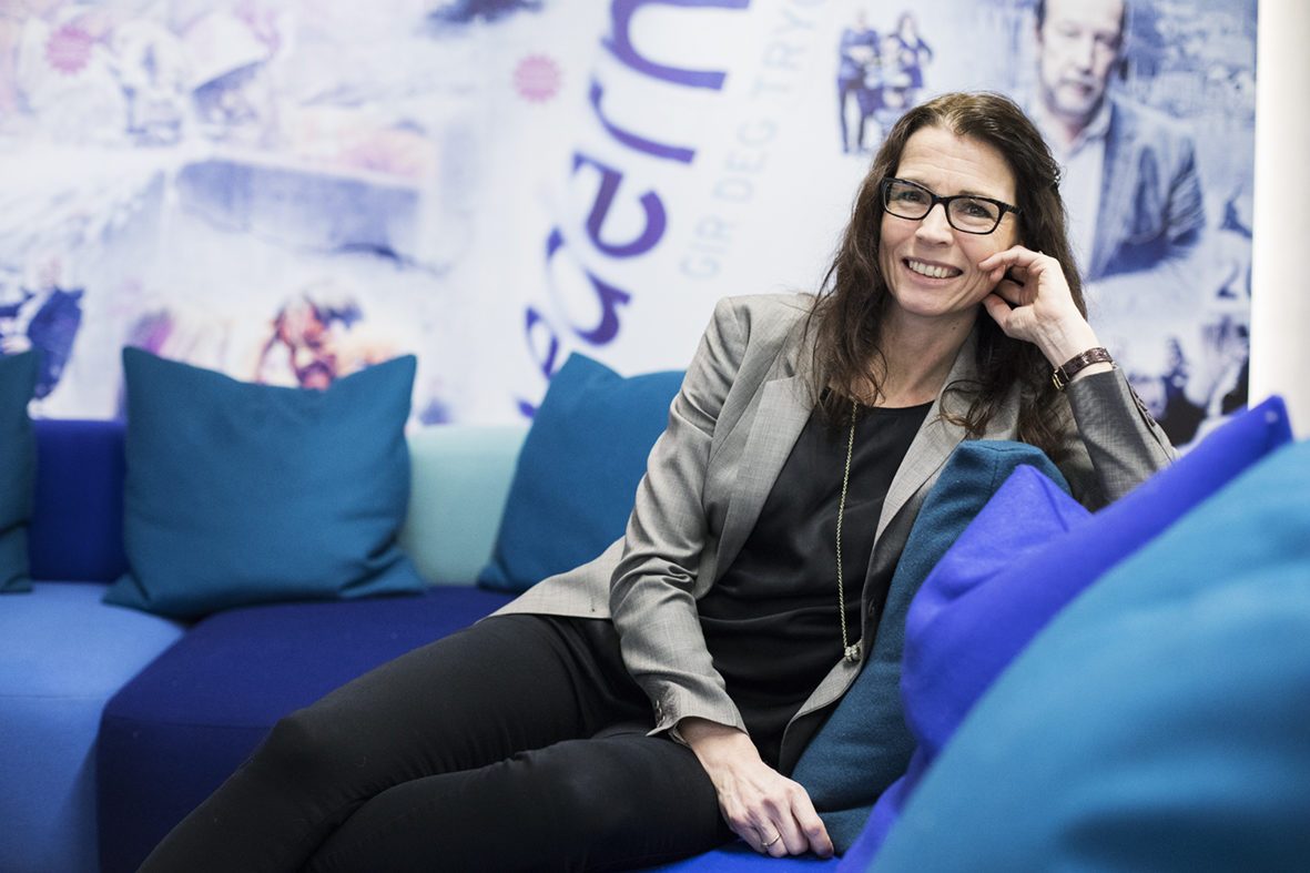 Suksess: Kvinne med langt brunt hår, briller og grå blazer sitter i en fargerik sofa.