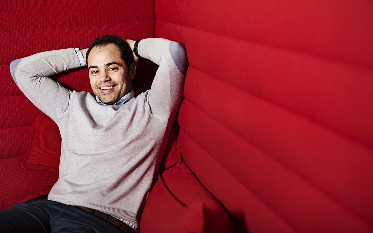 Integrering og inkludering: Mann med grå genser sitter tilbakelent i en stor, rød sofa.