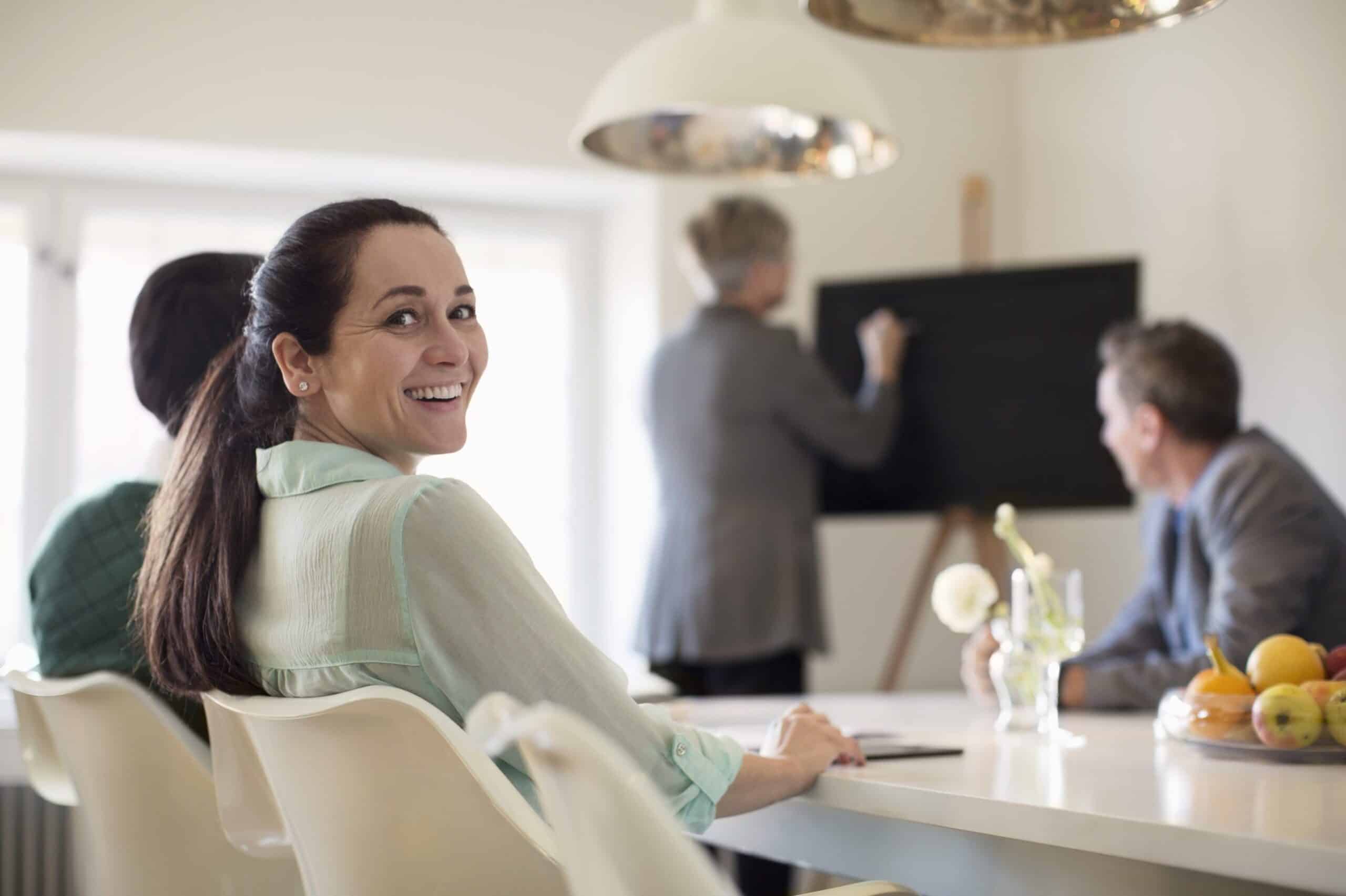 Jobbsøknad: Er hun den rette? Kvinne med langt mørkt hår sitter i et møte. Hun snur seg mot kameraet og smiler.