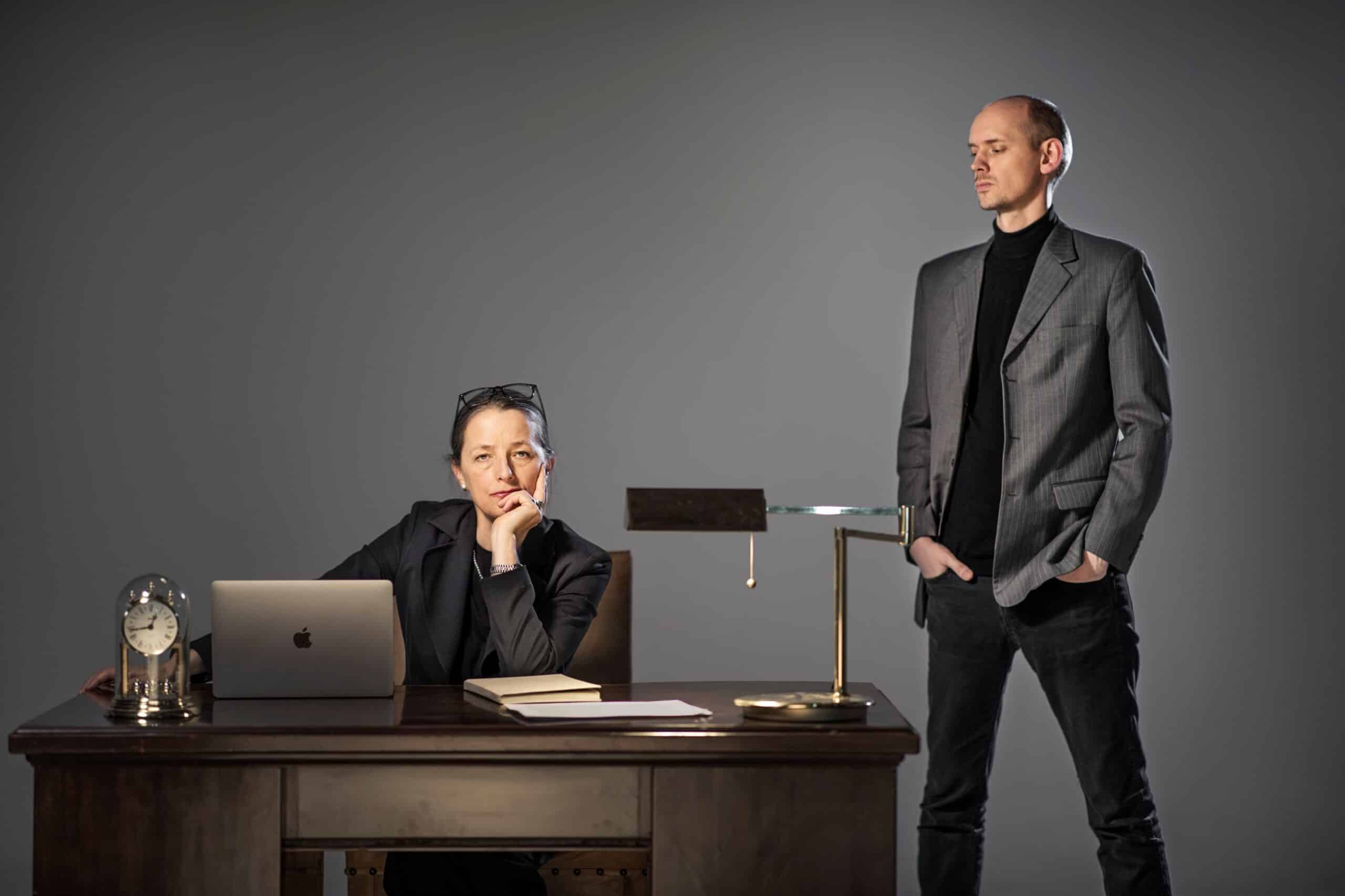 Frykt på jobben: Streng kvinne siter bak et gammelt skrivebord, en nedlatende mann står ved siden av.