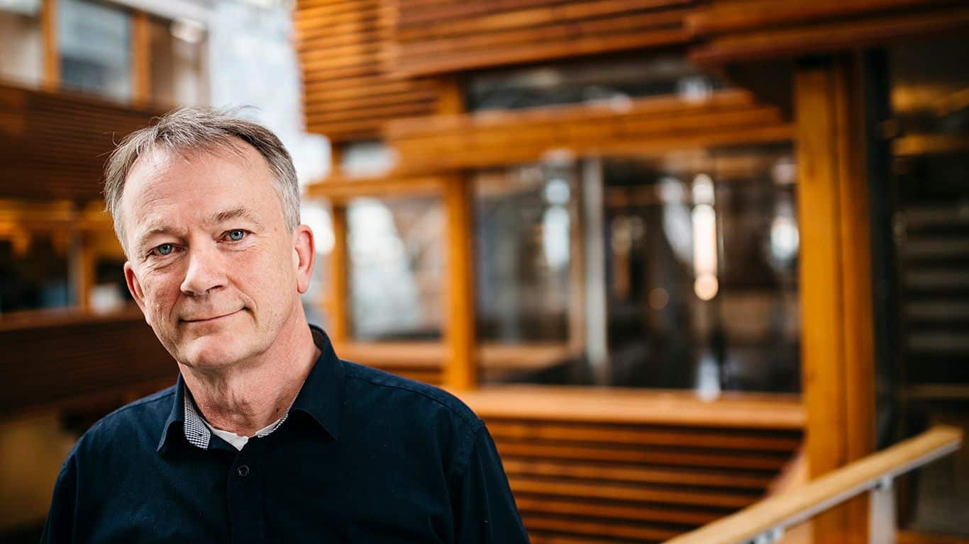 Organisasjon: Mann står i et interiør preget av glas og treverk.