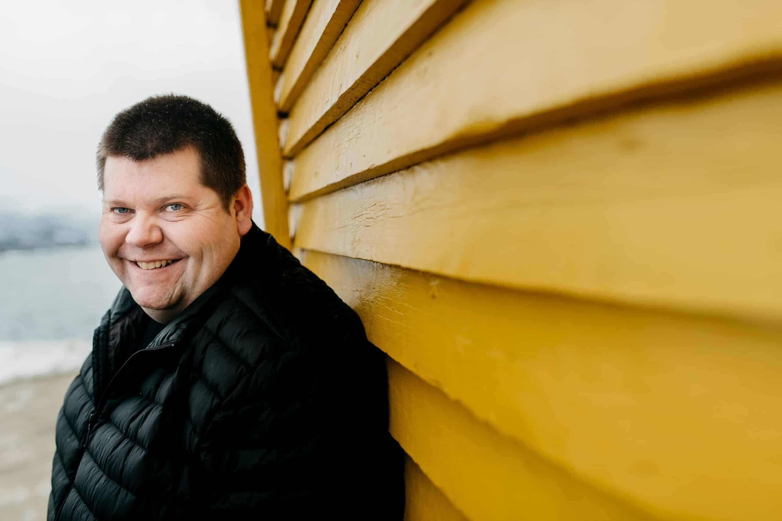 Salangen Nyheter: Blid mann lener seg mot gul trevegg.