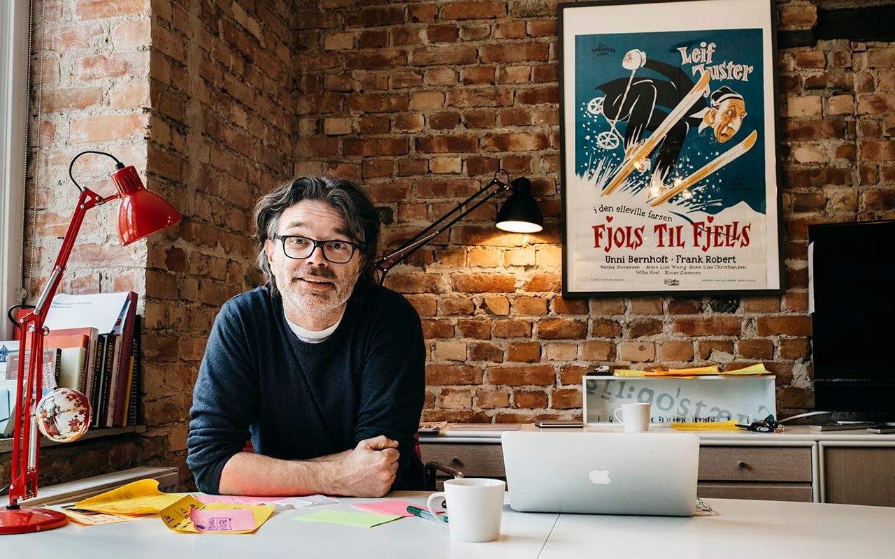 Nysgjerrig: Mann siter ved et skrivebord med en Fjols til fjells-plakat på veggen bak seg.