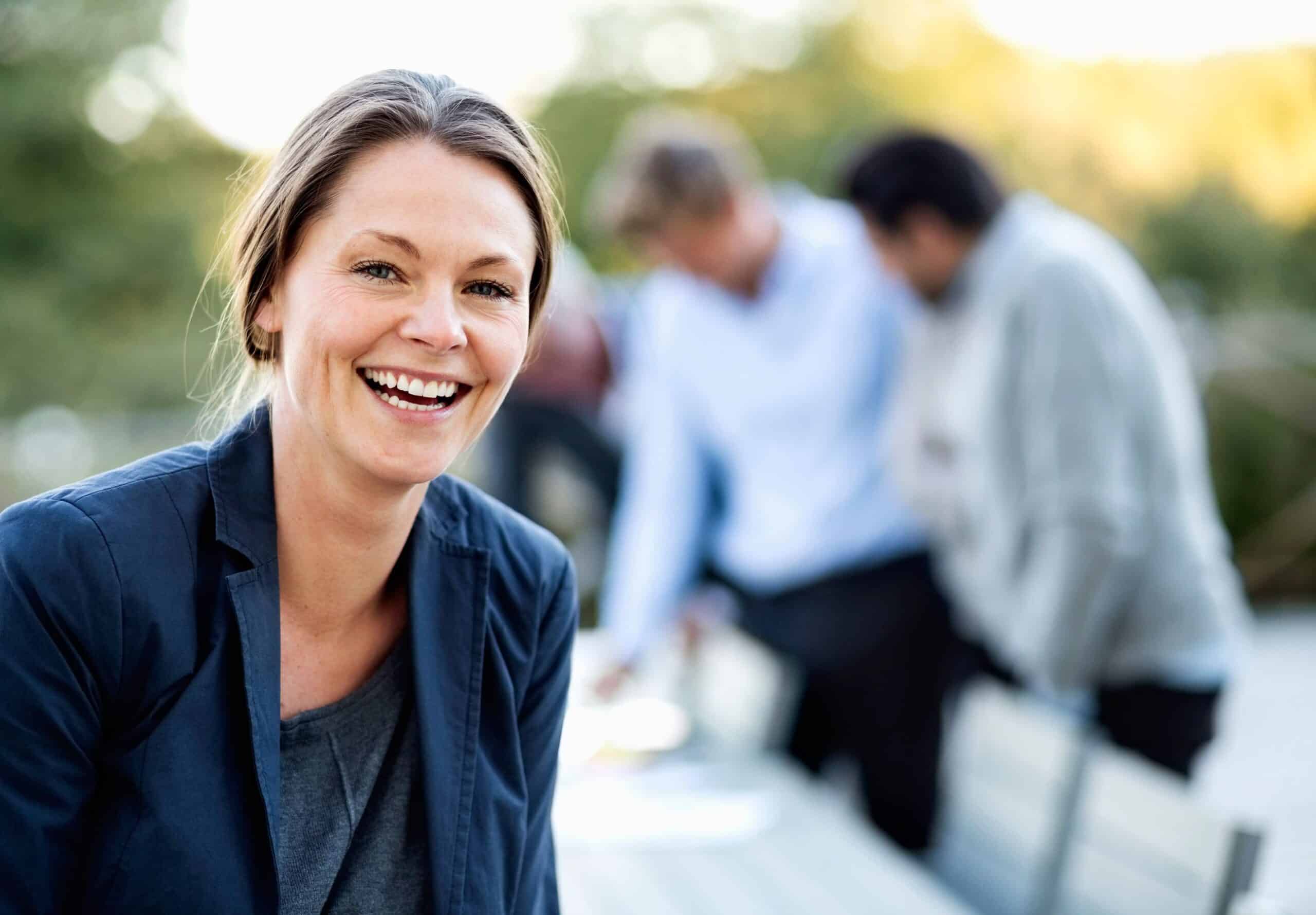 Jobbintervju: Blid kvinne smiler med et par menn i bakgrunnen.