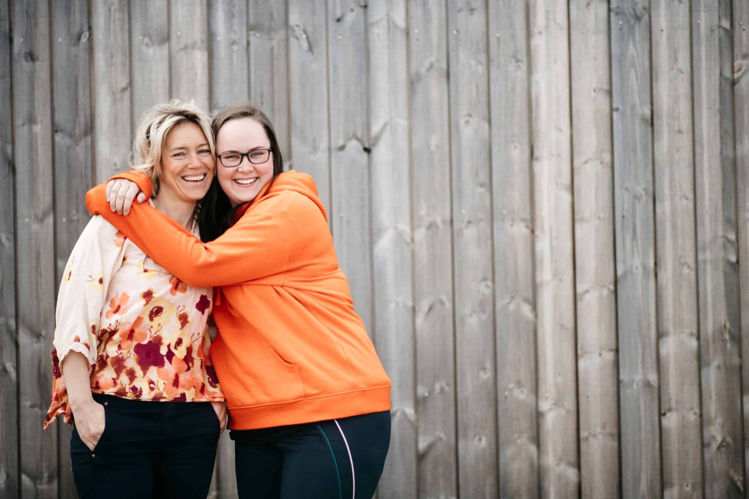 IA-bedrift: To blide kvinner foran en vegg, den ene holder omkring den andre.