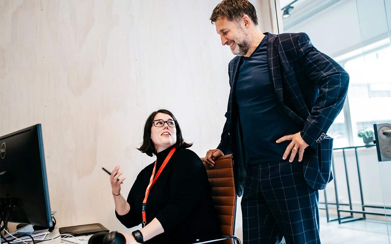 Verdier: En kvinne sitter foran PC-en og ser opp på en mann.