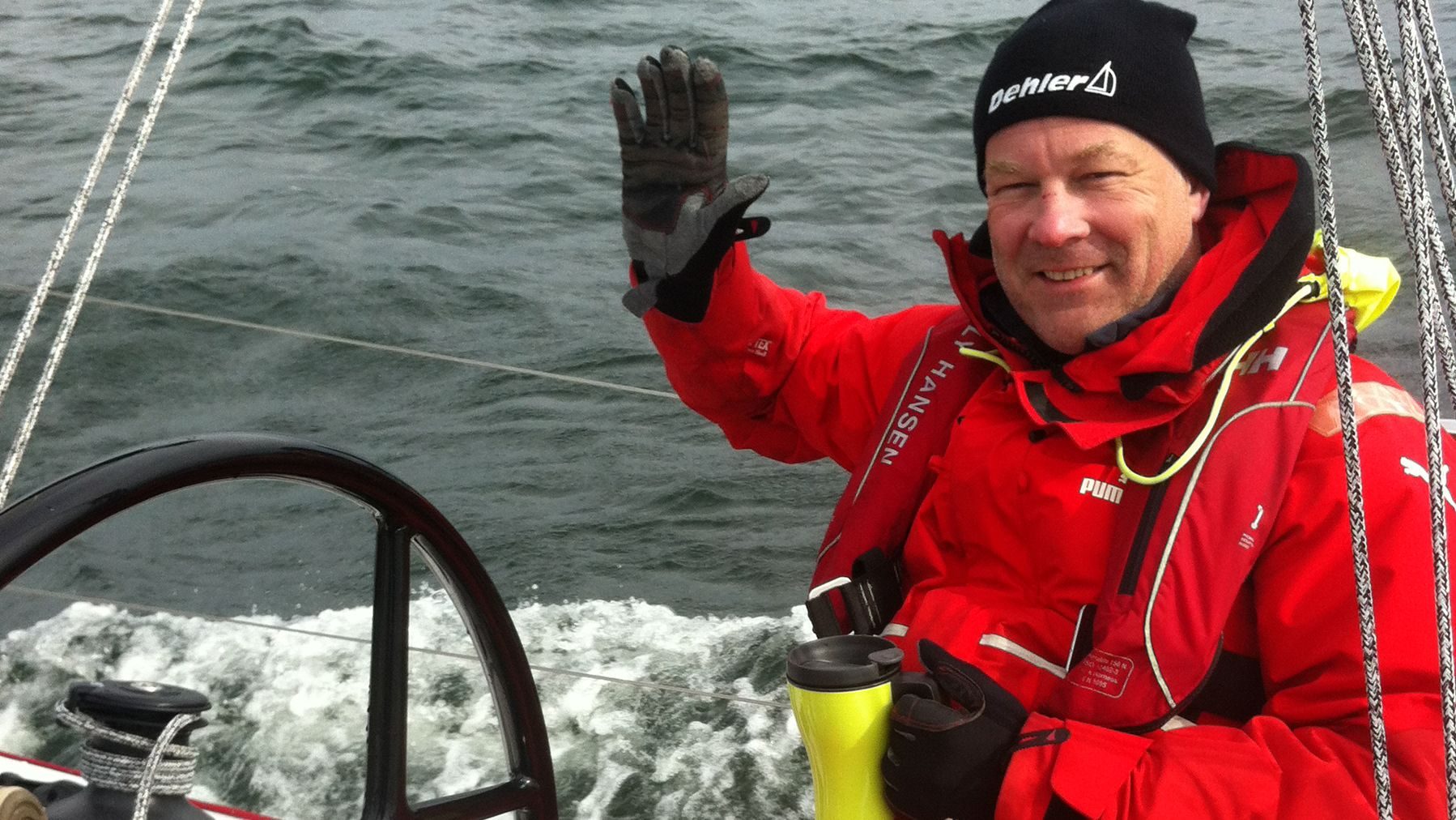 Nysgjerrig: Mann i røde seilerklær sitter og vinker i en seilbåt.