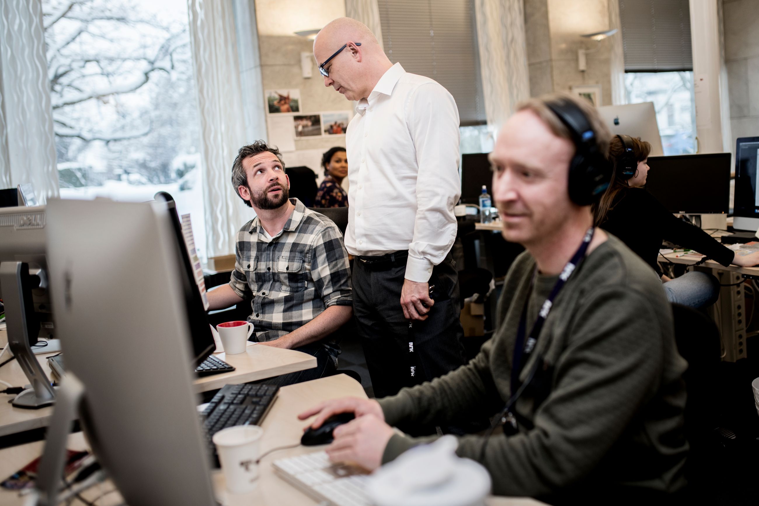 Nysgjerrig: Mann i hvit skjorte besøker en redaksjon der to menn sitter og jobber.