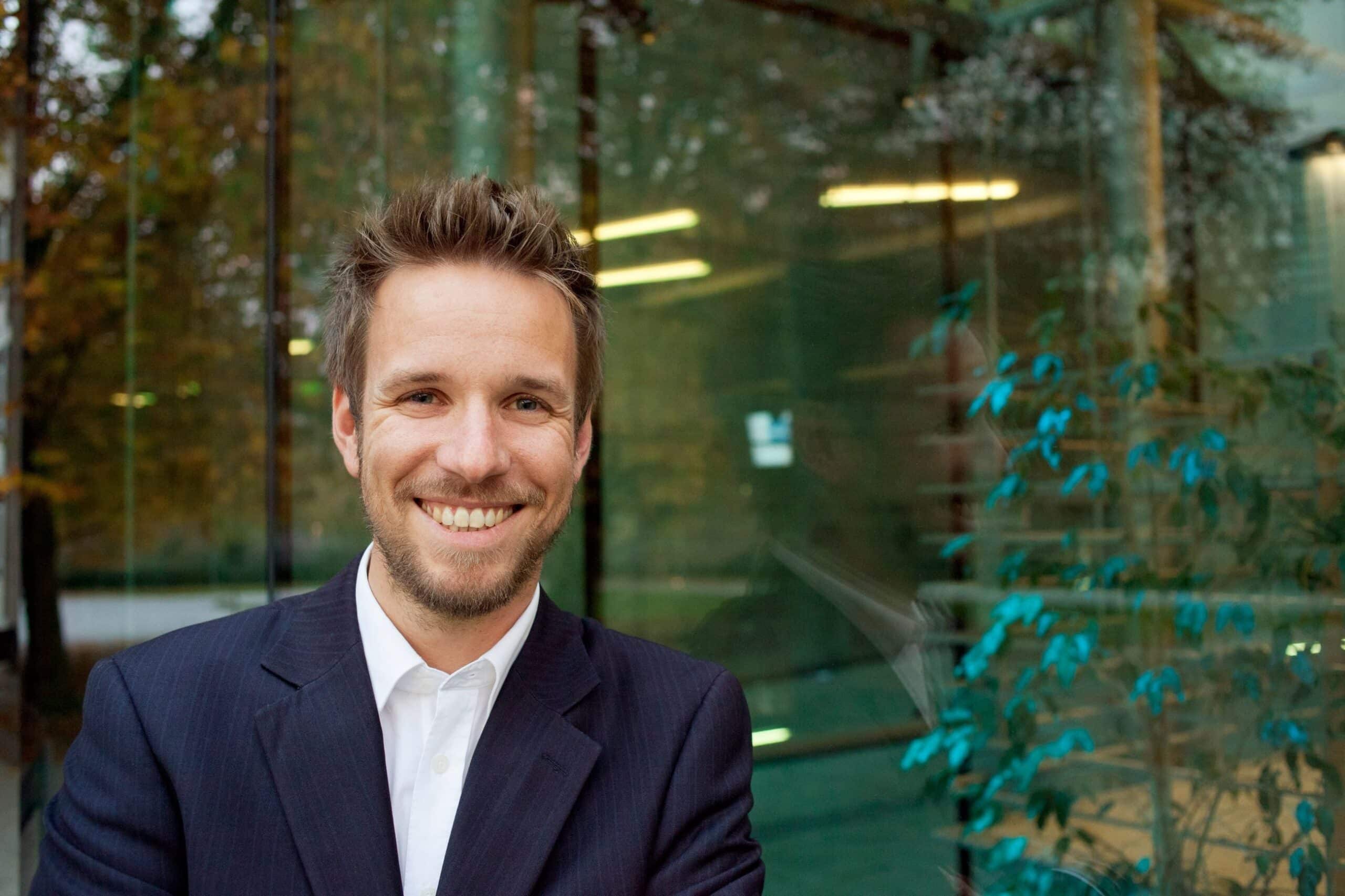 Lykkes: Blid mann med skjegg står foran et vindu.