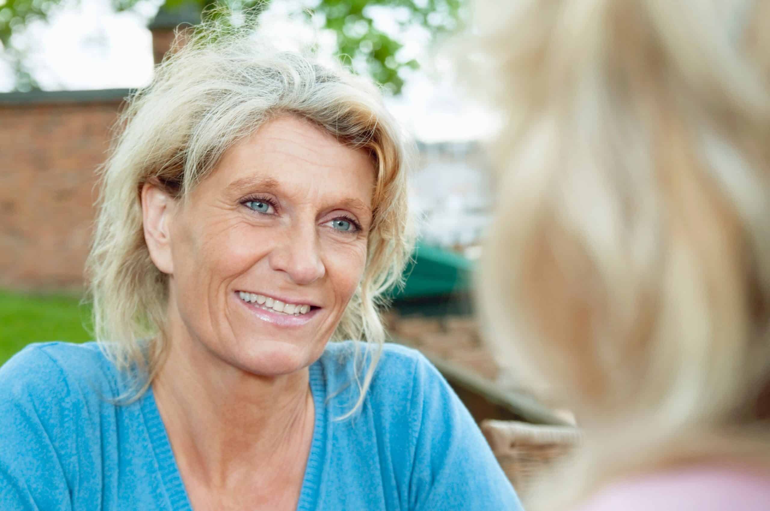 Læring: Blond, godt voksen kvinne smiler til en annen person vi bare ser litt av.