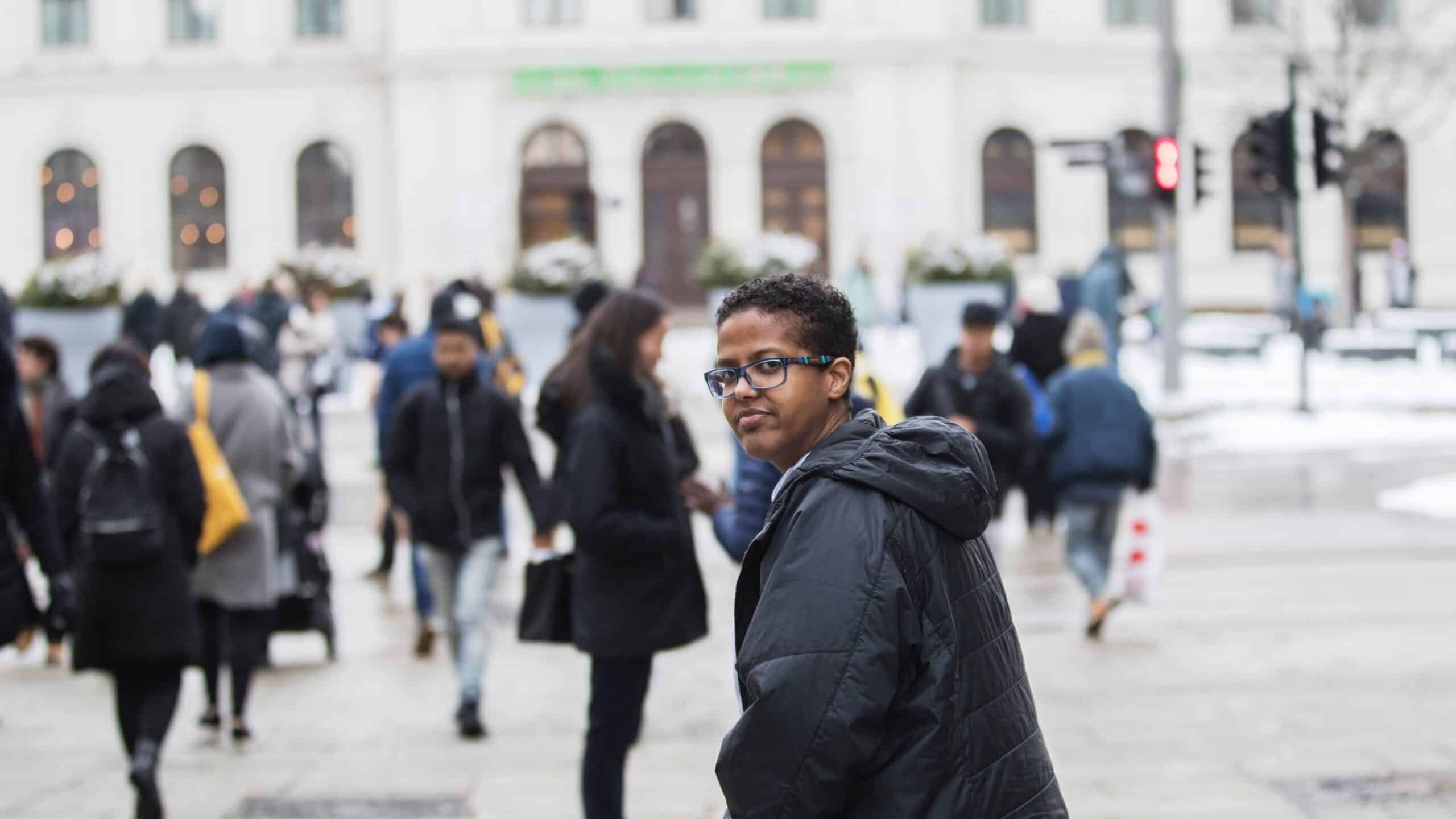 Likestilling: Mørk kvinne med blå jakke står på sjøsiden av Østbanehallen, med mange mennesker rundt seg.