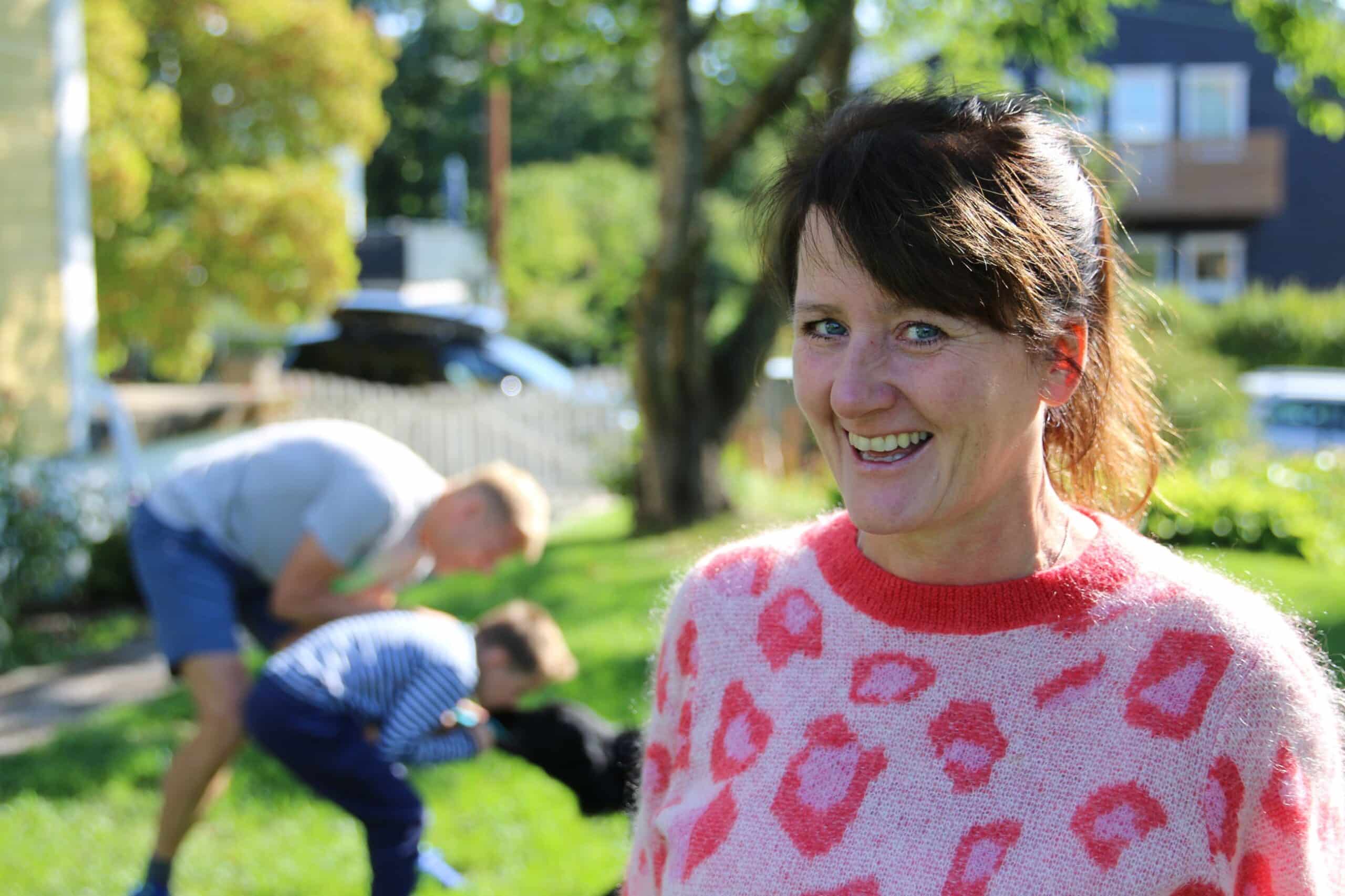 Karriere: Blid kvinne i forgrunnen, med mann og et barn som leker i bakgrunnen.