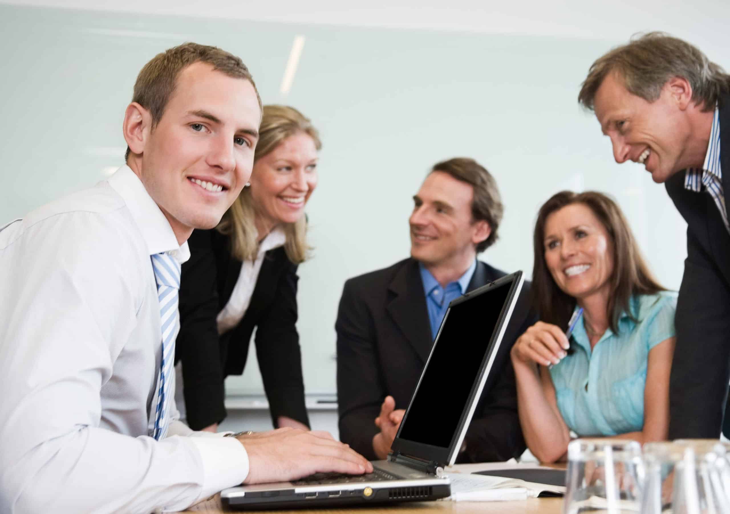 Anerkjennelse: Tre menn og to kvinner i en god situasjon på jobben, samlet rundt et bord.