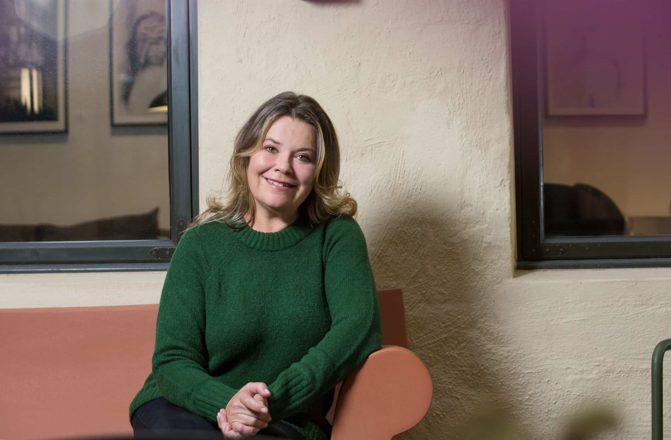 Verdier: Kvinne i grønn genser sitter i en sofa og smiler mot kameraet.