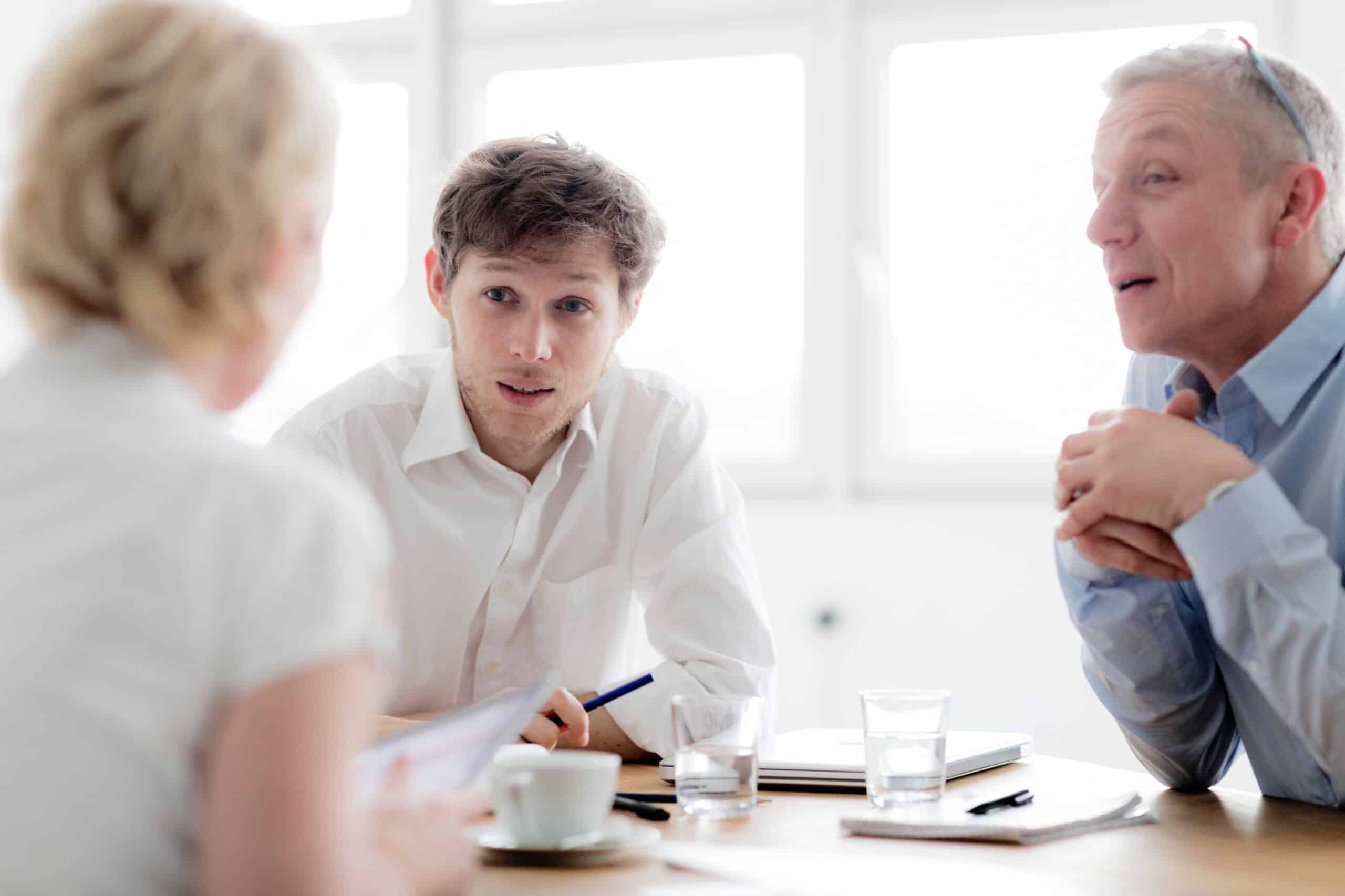 Personligheter: En kvinne og to menn snakker sammen rundt et bord. Kvinnen sitter med ryggen til.