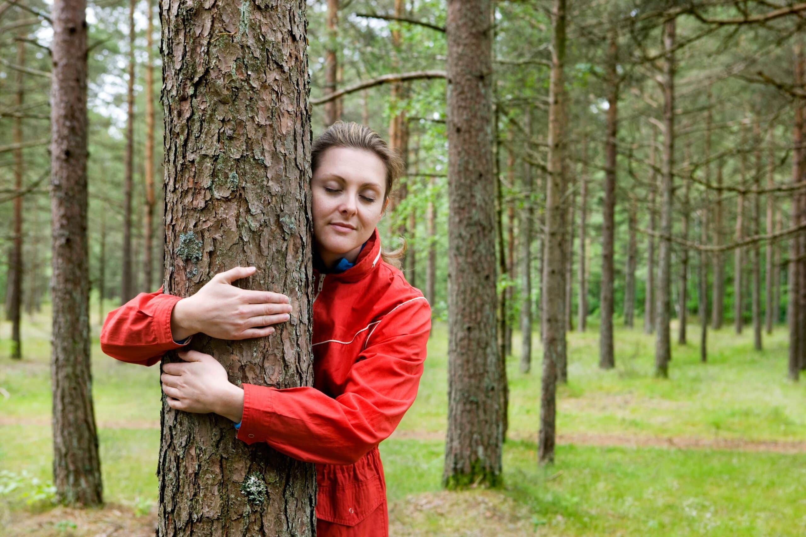 Balanse: Kvinne med rød ytterjakke omfavner et tre i skogen.