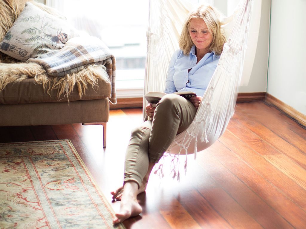 Endring: Blond kvinne sitter og leser i en stol som henger fra taket.