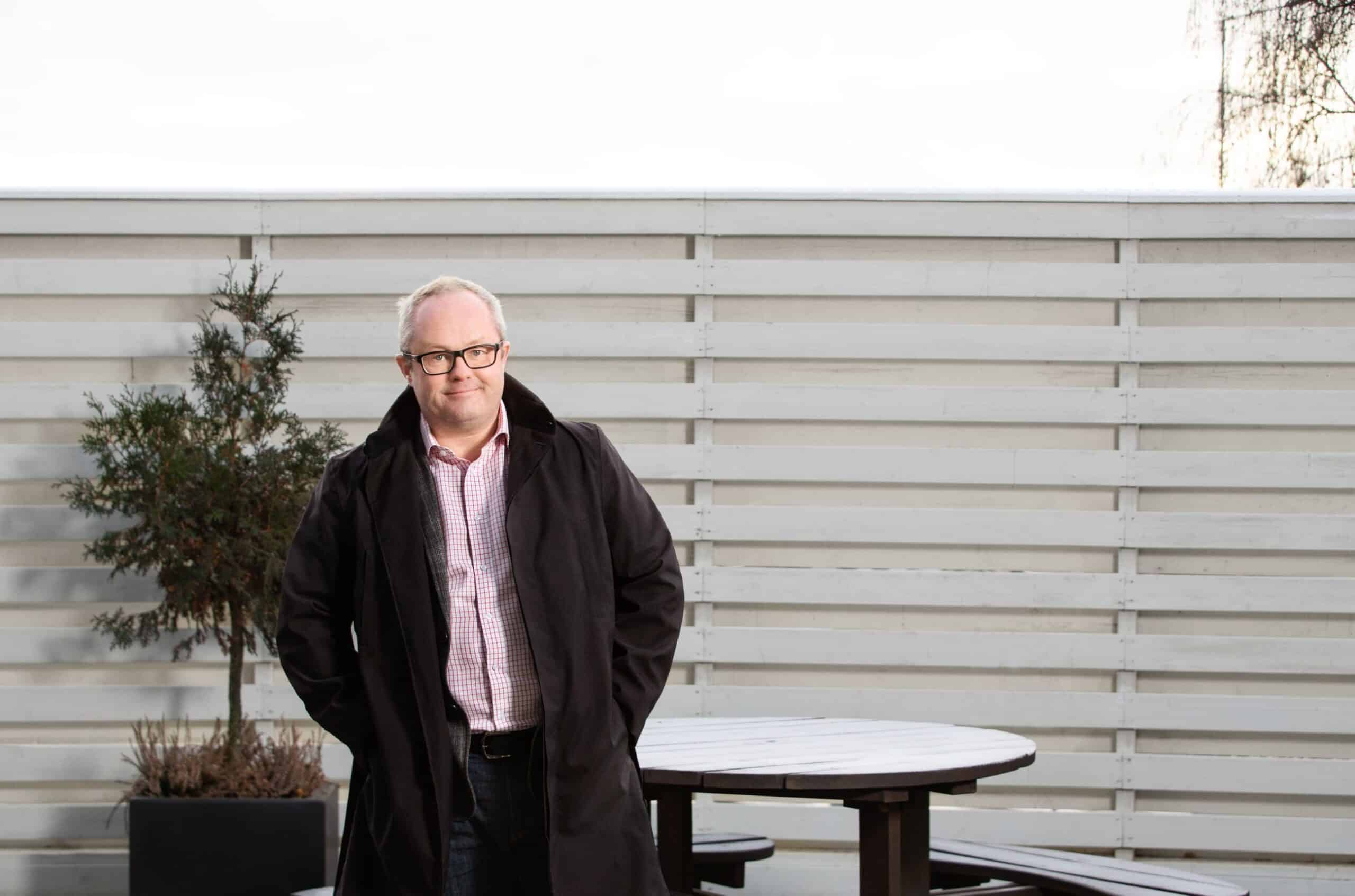 Sykefravær: Mann i frakk står foran en levegg.