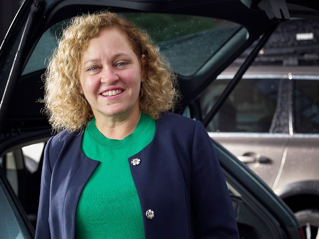 Nettverk: Kvinne med krøllete hår står foran en bil.