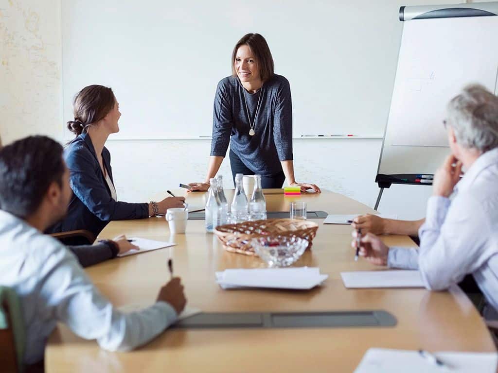 Endringene: En kvinne står foran noen kolleger og snakker ved et bord.