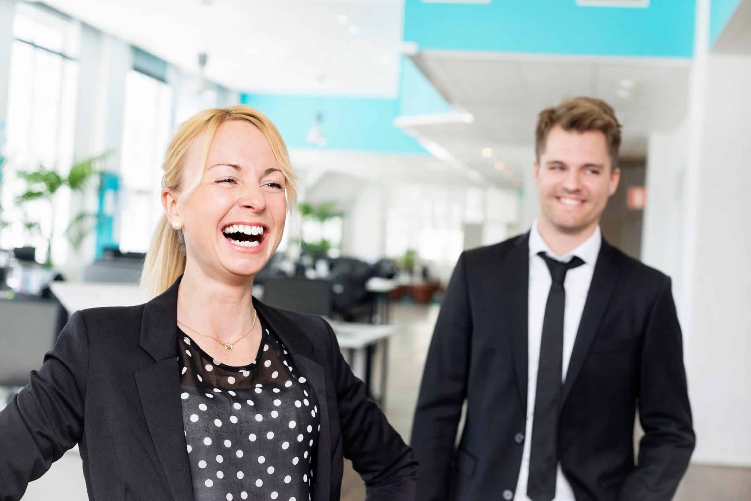 Motivasjon: En kvinne ler og en mann smiler i et kontorlandskap.