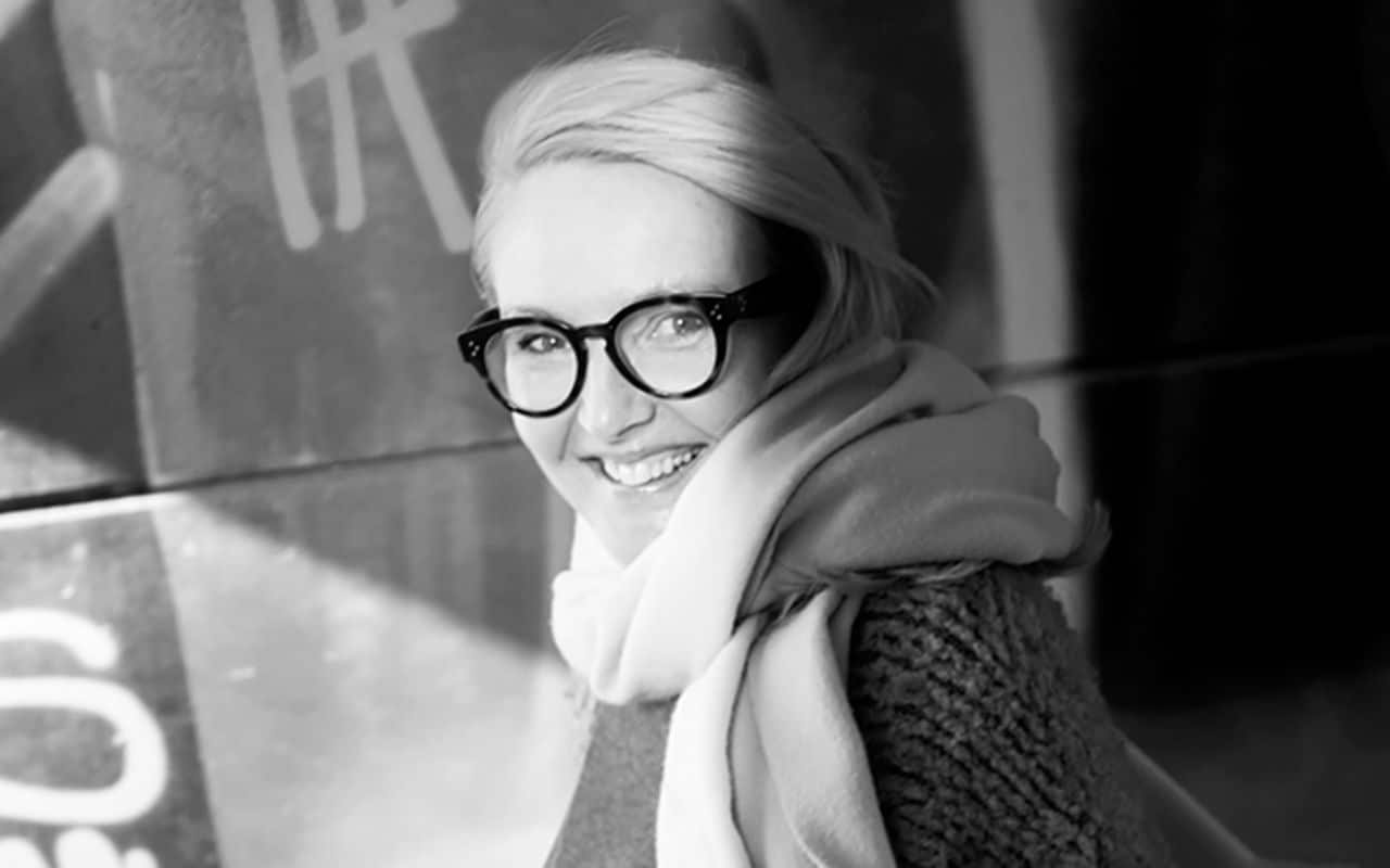 Stillhet: Kvinne med briller smiler til kameraet i forbifarten.