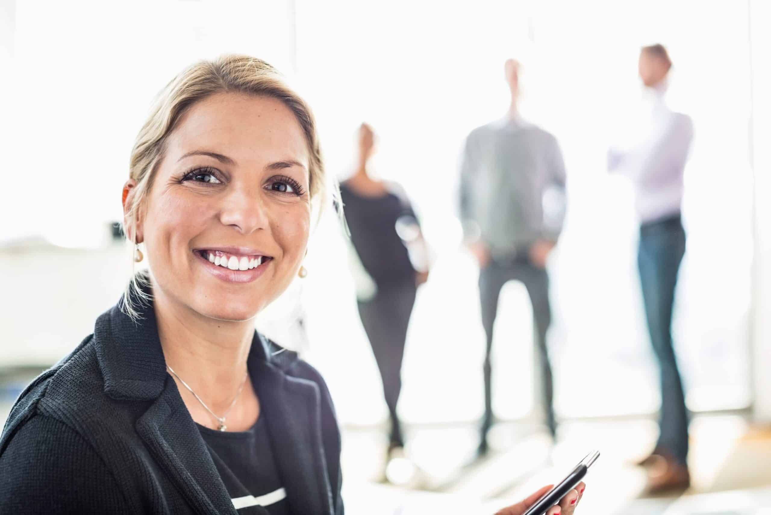 Påvirkning: Blid kvinne ser rett i kameraet, i bakgrunnen anes tre mennesker.