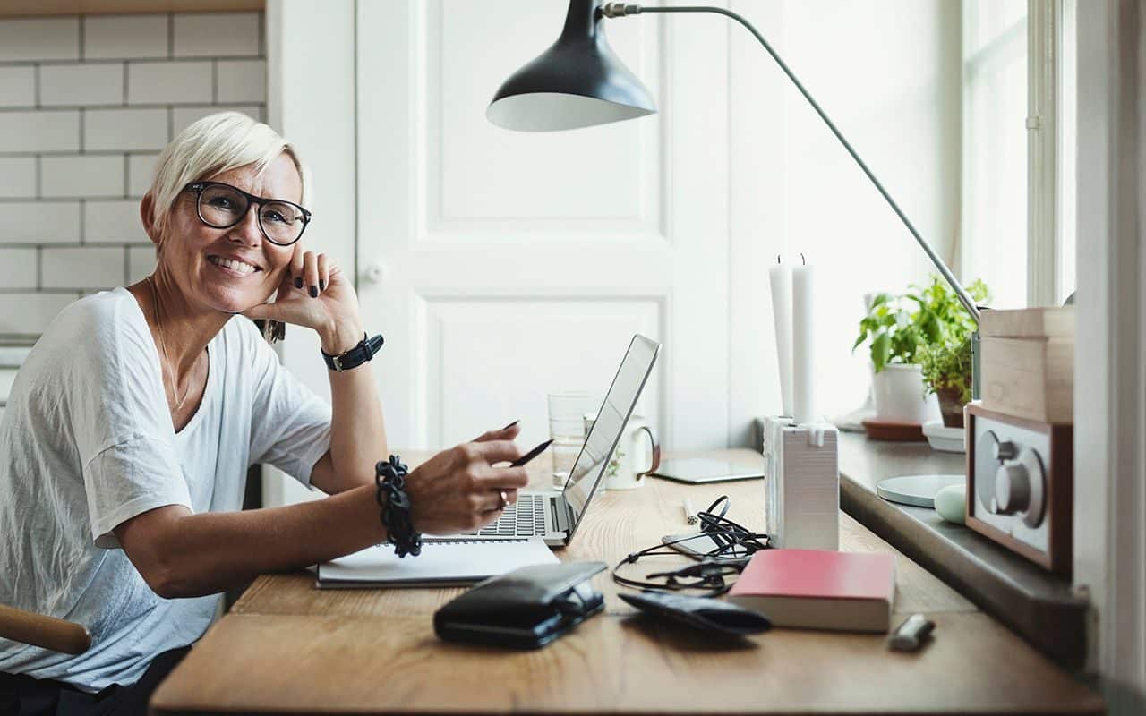 Fleksibilitet: Blid kvinner sitter og jobber hjemme med PC-en foran seg.