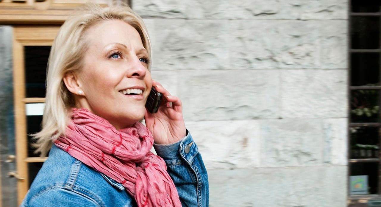 Fleksibel: Blid kvinne snakker i telefonen utendørs.