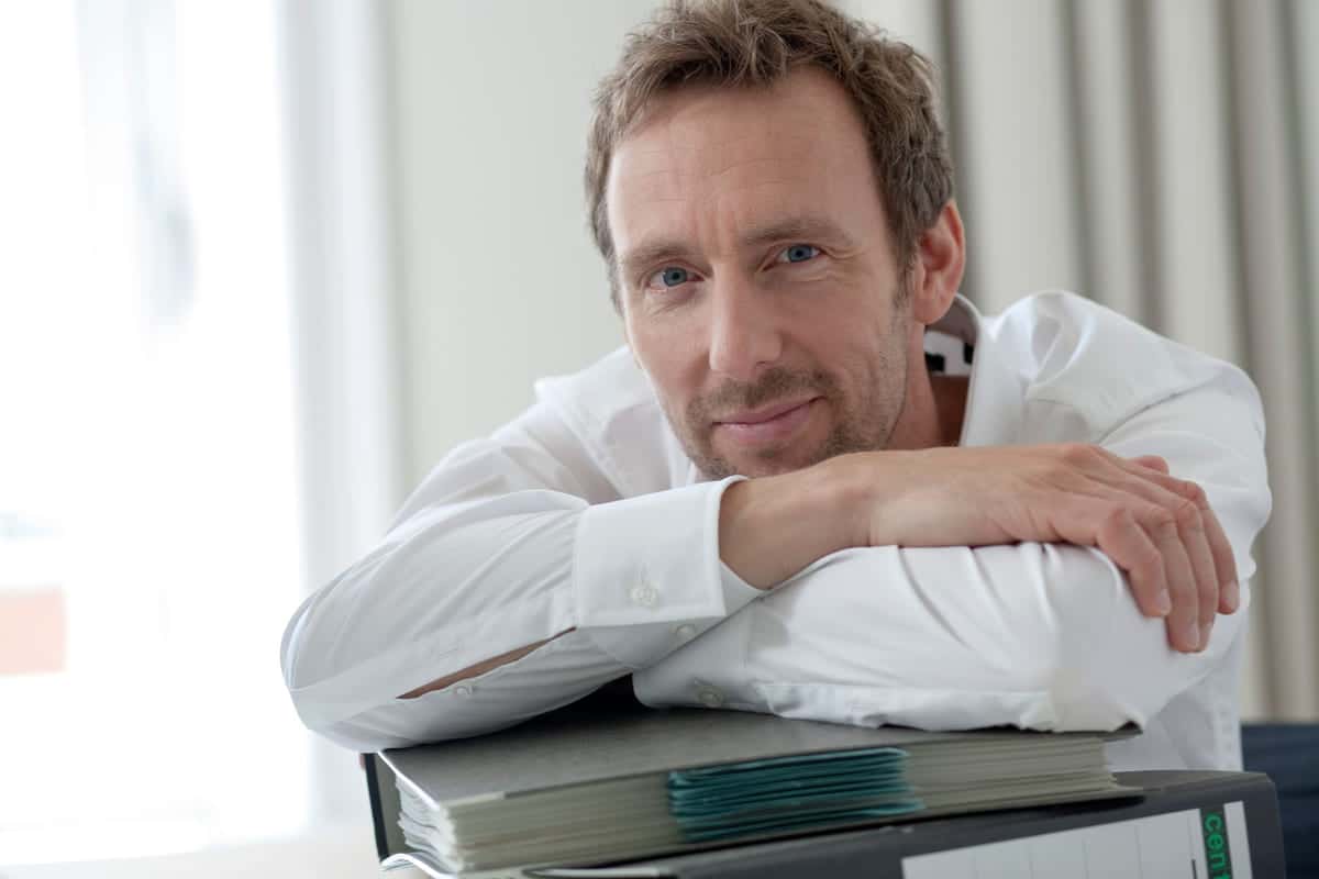 Trygghet: Mann i hvit skjorte lener seg over en bunke og ser i kameraet.