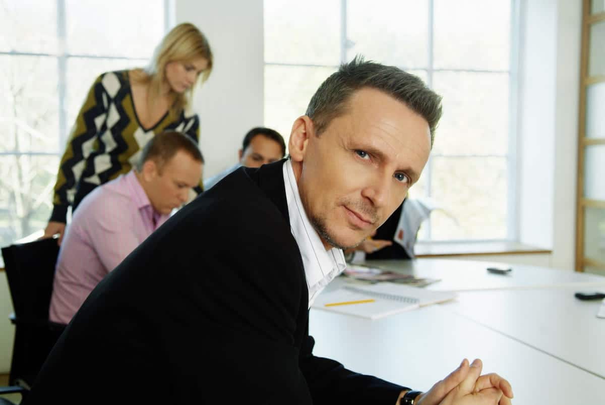 Engasjement: Mann sitter i forgrunnen ved et møtebord, kolleger i bakgrunnen.