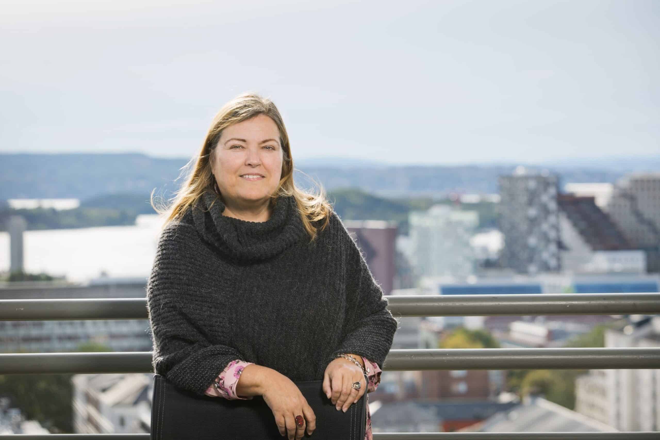 Seniorer: Kvinne står på en takterrasse med grå poncho på seg.