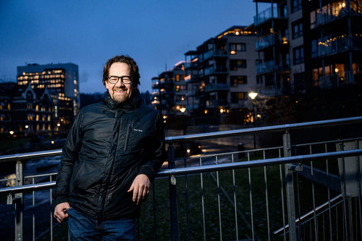 Ledere: Blid mann står utendørs med boliger i bakgrunnen, tidlig om morgenen.