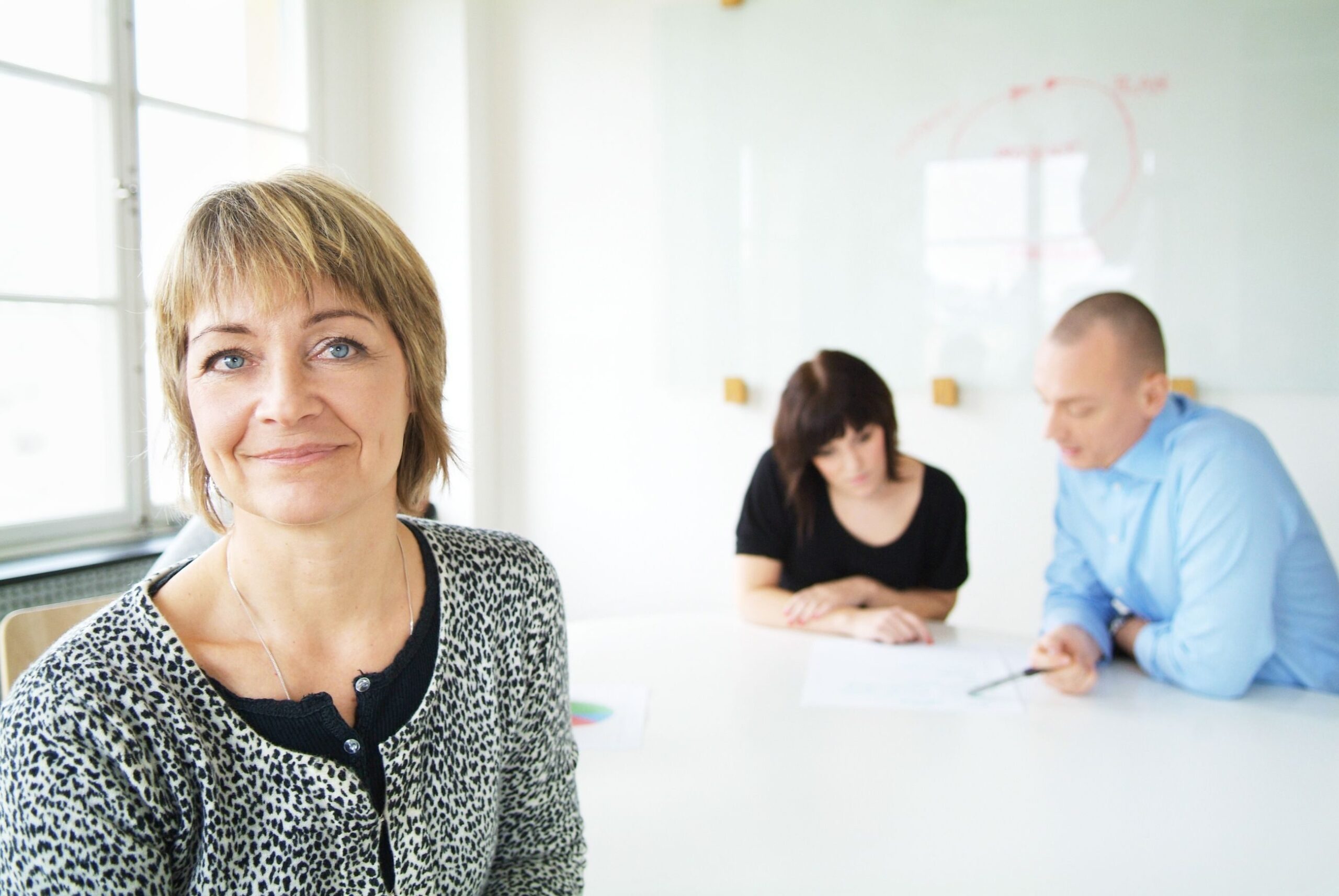 Positiv: Kvinne i forgrunnen smiler, bak ses en kvinne og en mann ved et bord.