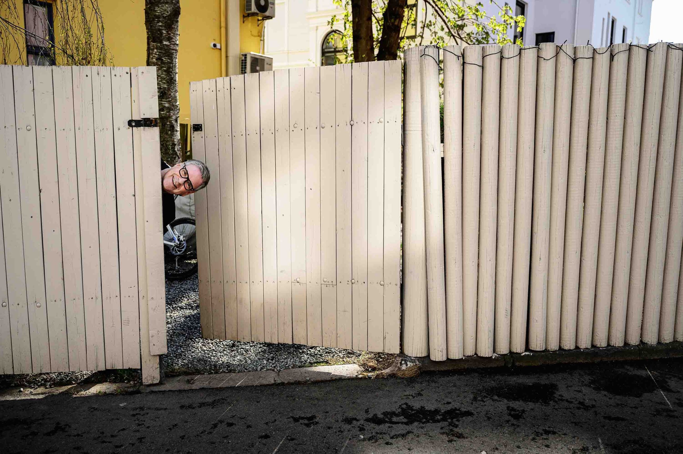 Jon Morten Melhus som titter ut fra bak et høyt gjerde og smiler