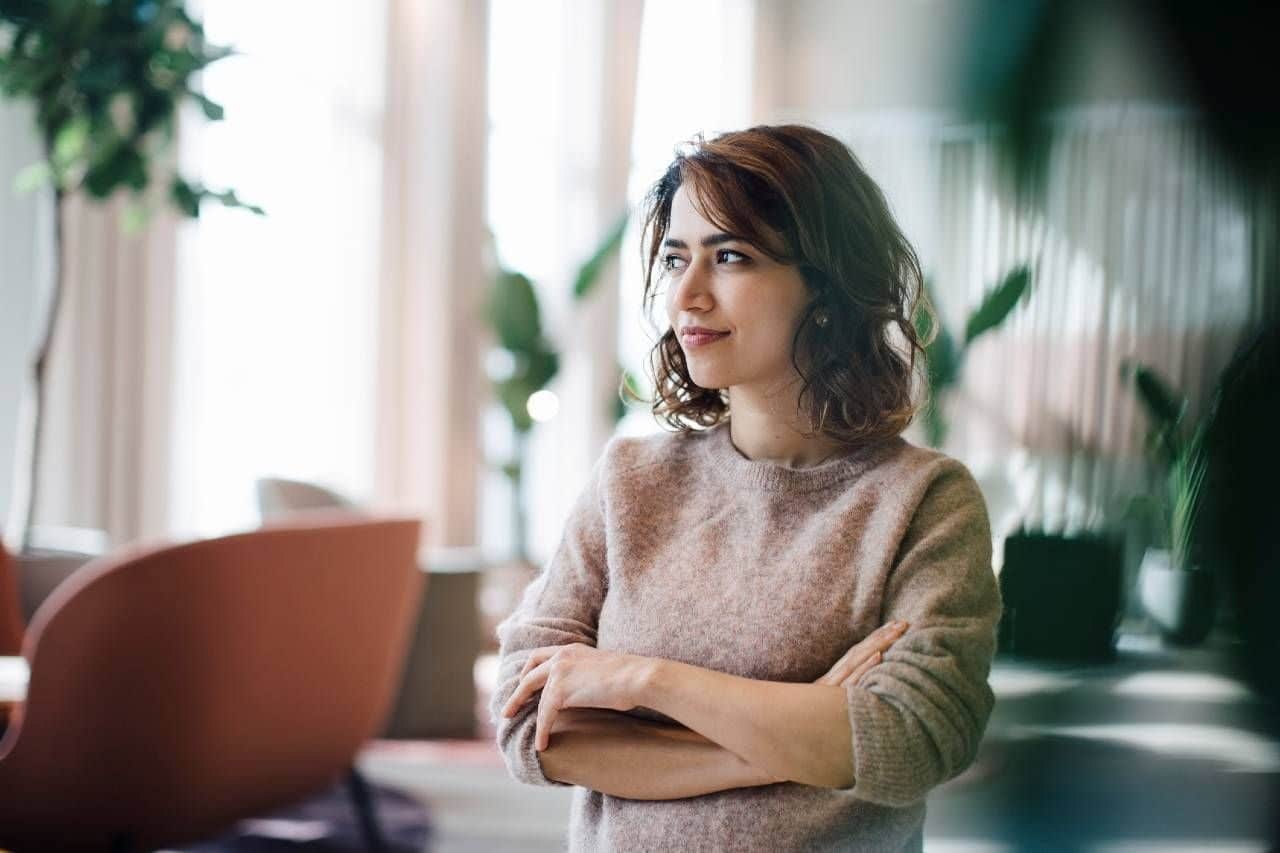 Kvinne med langt brunt hår står med armene i kors og ser ut i rommet. Bilde til sak om psykososialt arbeidsmiljø for Lederne