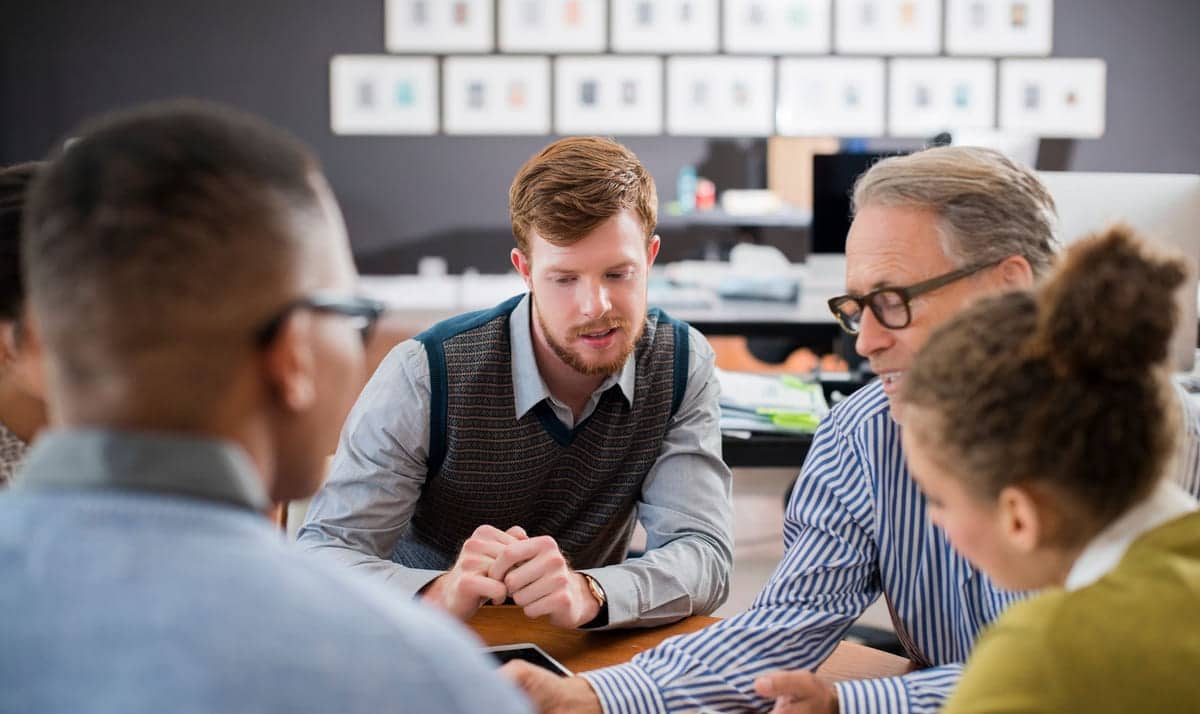 Fire kollegaer sitter rundt et bord. Businessmann delegerer opggaver