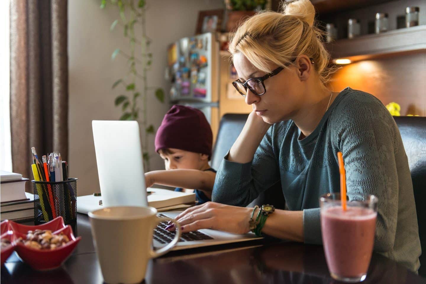Kvinne som jobber overtid på hjemmekontor med sønnen ved siden av seg