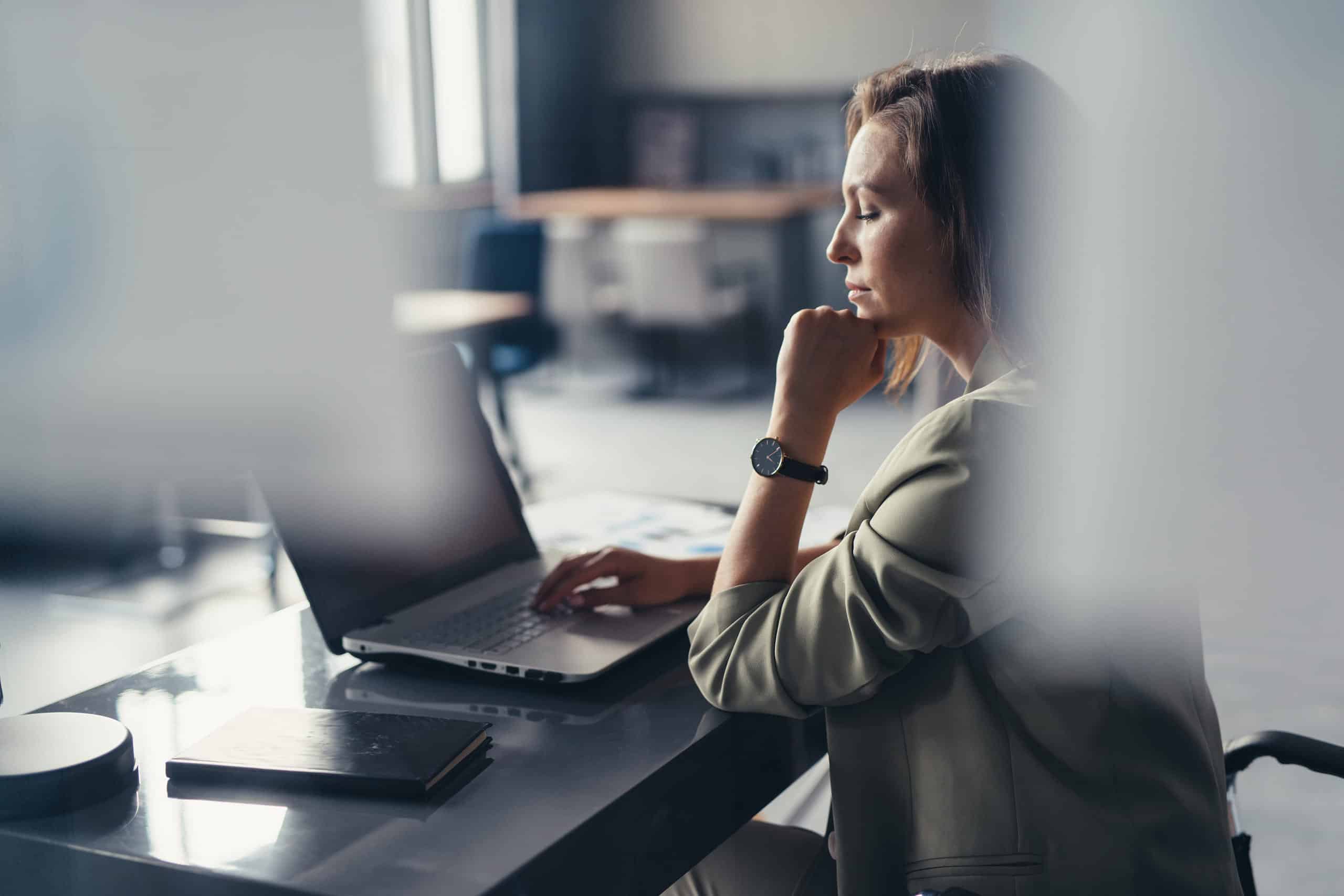 En dame som sitter ved en bærbar pc, tenker på sin skriftlige kommunikasjon