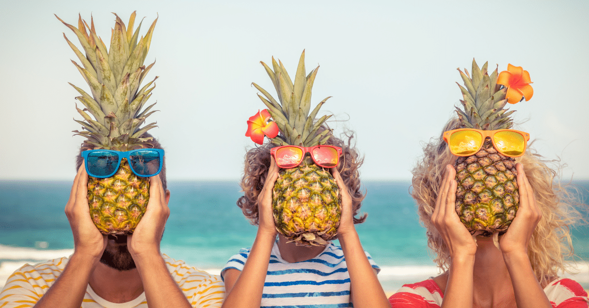 Tre mennesker som holder en ananas med solbriller foran fjeset