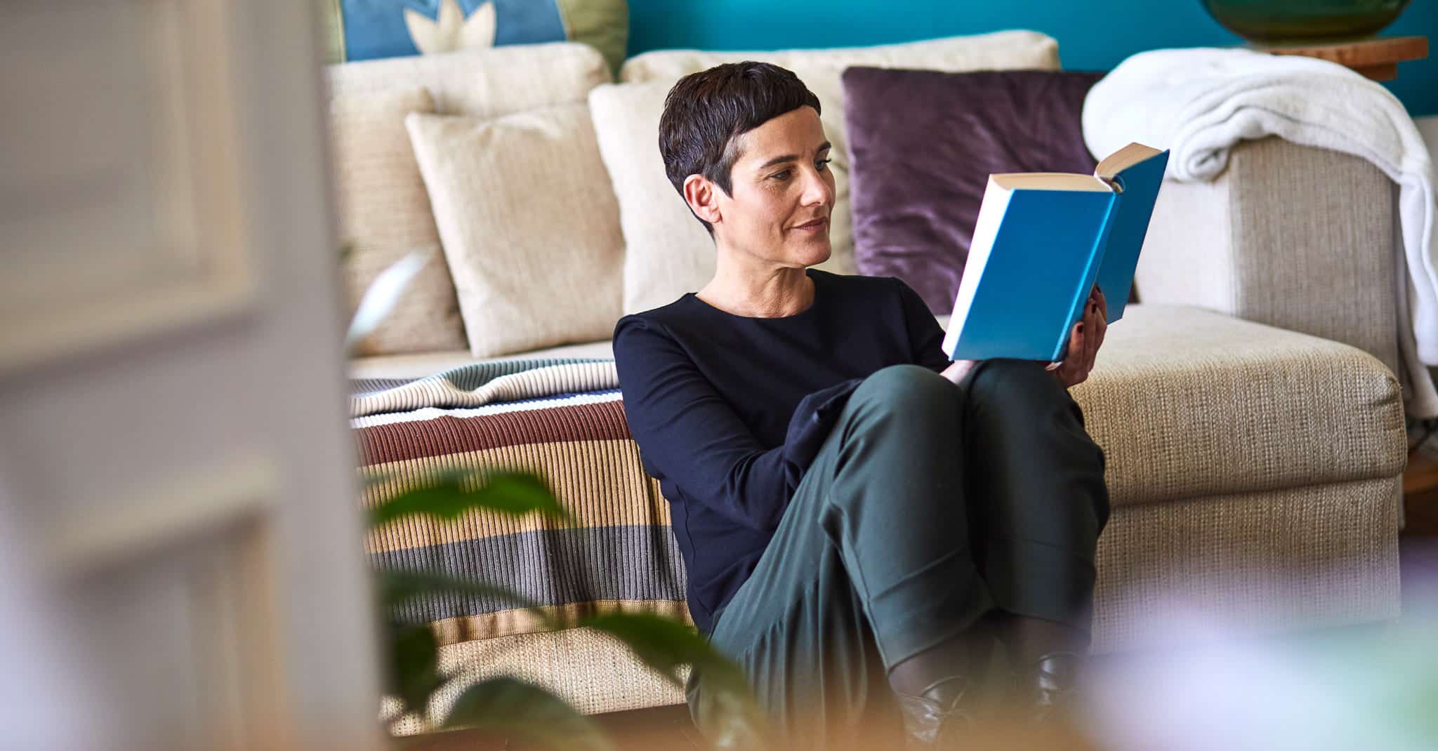 En dame sitter hjemme og leser en bok.