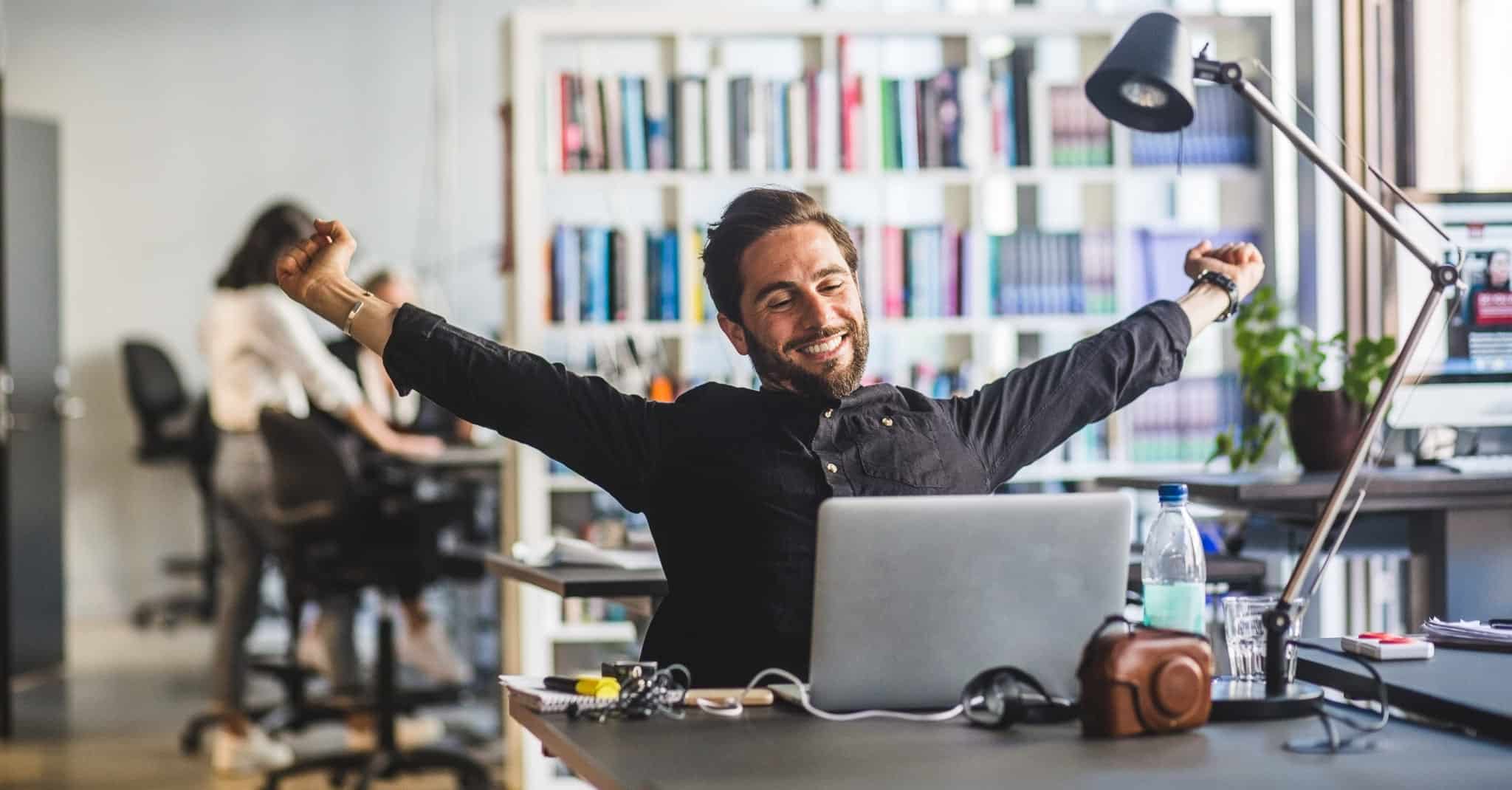 En mann strekker henda i været ved kontorpulten.