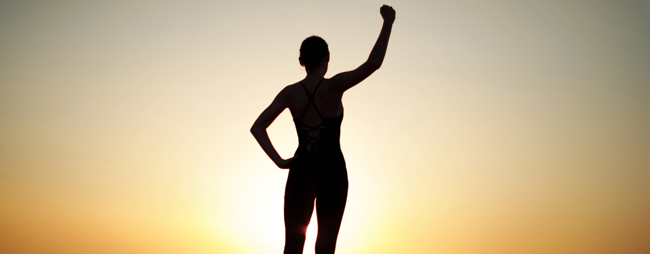 Kvinne står med armen hevet i solnedgang