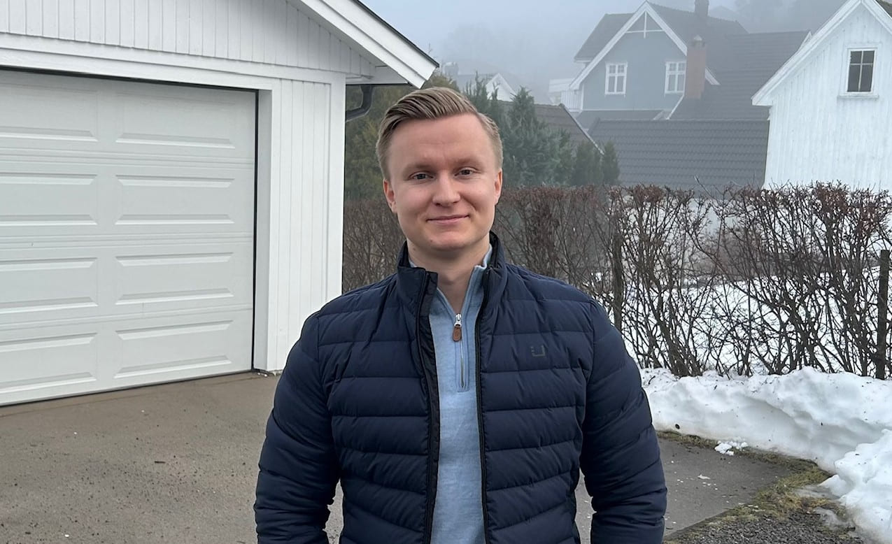 Marius Eliassen smiler til kamera stående foran en garasje