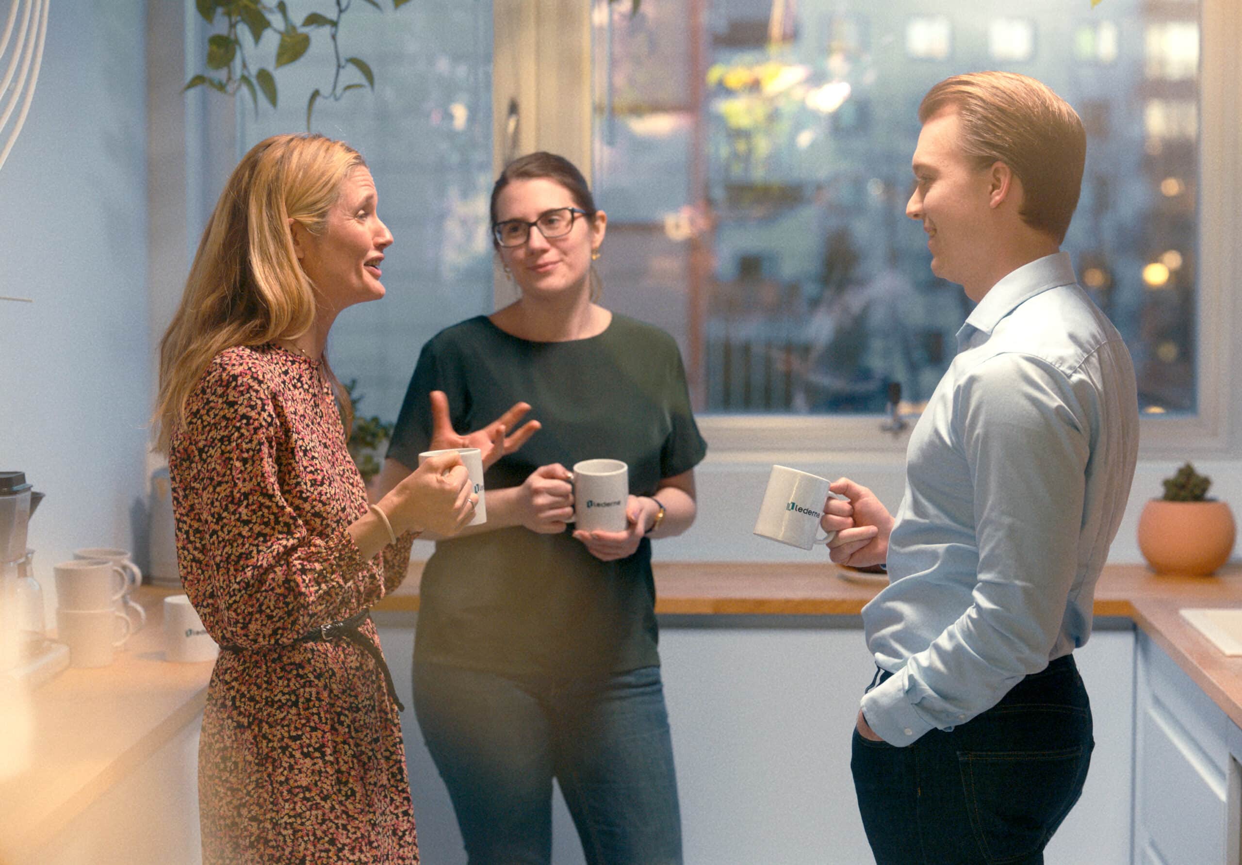 Tre mennesker snakker og drikker kaffe på jobb