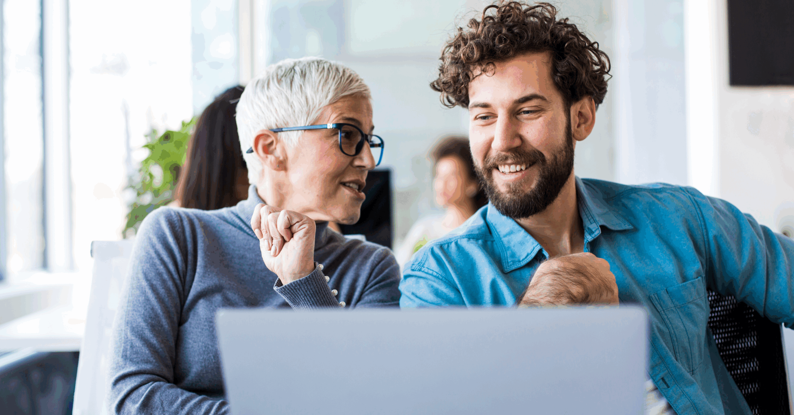 En eldre dame og en ung mann sitter foran en PC og har det hyggelig.